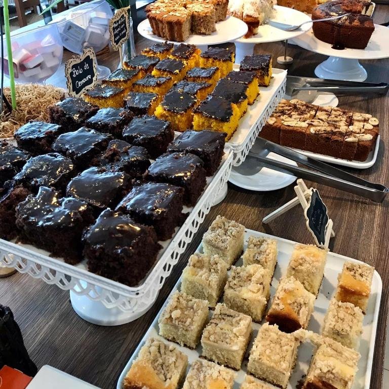 Bolos caseiros variados, com cobertura de chocolate e farofa, em suportes brancos