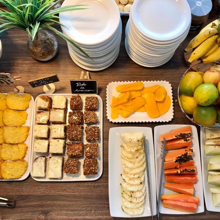 Mesa com travessas de bolos, frutas fatiadas e cesto de frutas no café da manhã