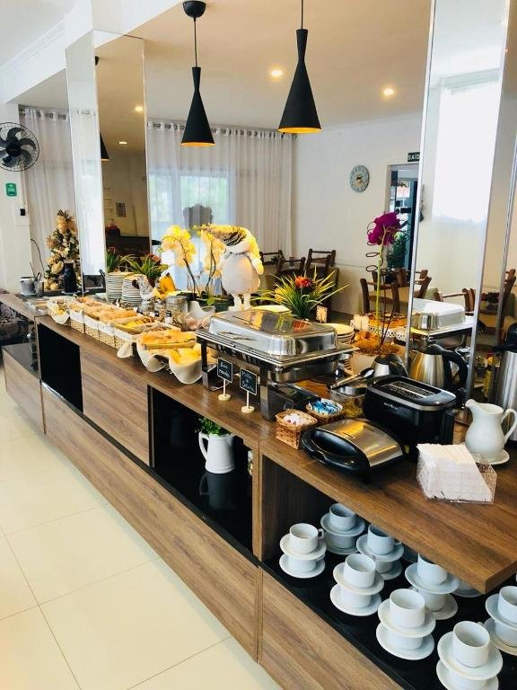 Bancada do buffet de café da manhã do Hotel Lorimar, com pães, bolos, rechaud e xícaras