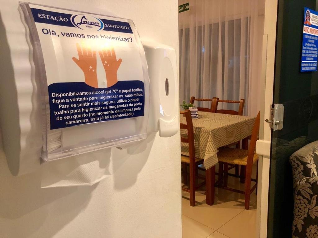 Estação de higienização com álcool em gel e papel-toalha junto ao salão de café da manhã