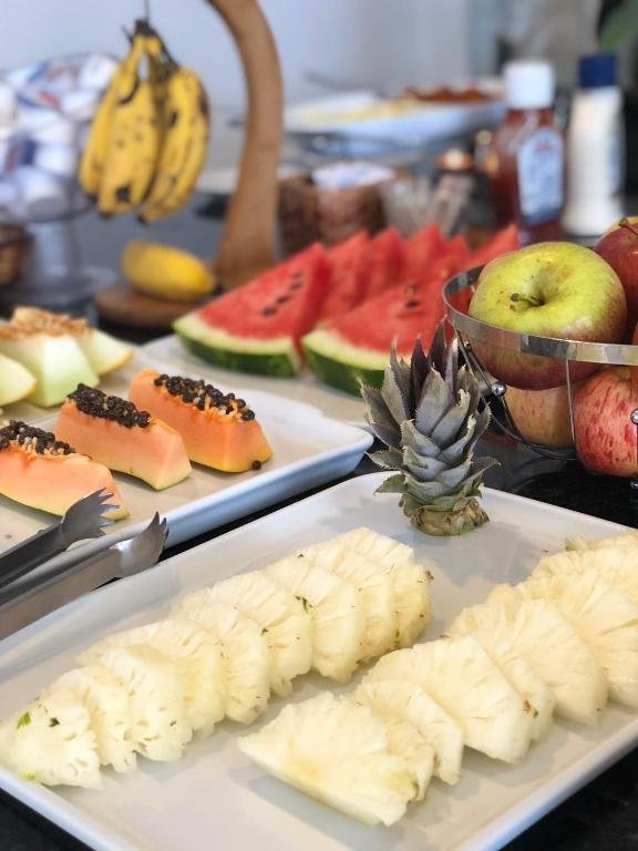 Travessas com abacaxi, mamão, melancia e melão fatiados e cesto de maçãs