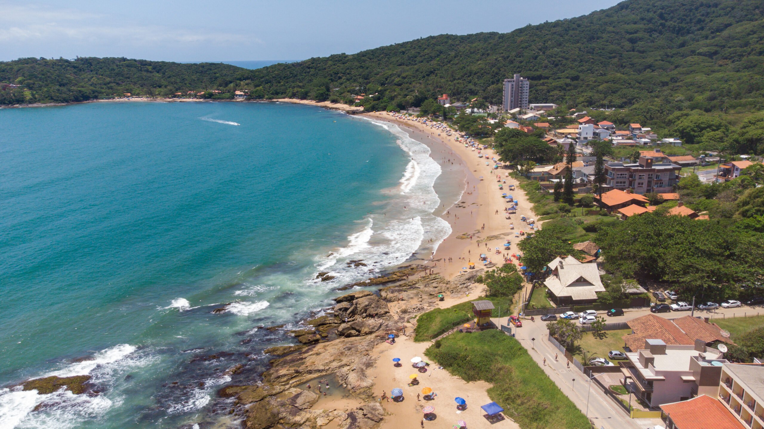 Vista aérea da Praia do Cerco, em Penha, com enseada de águas turquesa, costões rochosos e faixa de areia movimentada