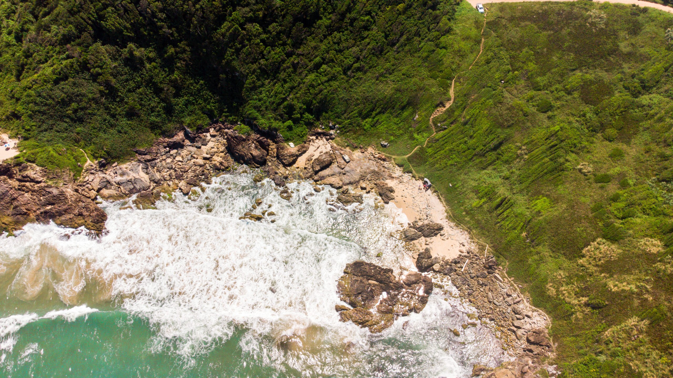Vista aérea da Praia do Marimbá, em Penha, uma enseada selvagem com costões rochosos e ondas batendo