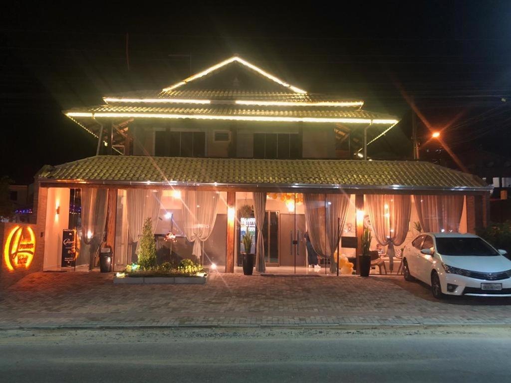 Fachada do Hotel Lorimar iluminada à noite, com luzes no telhado e cortinas nas janelas