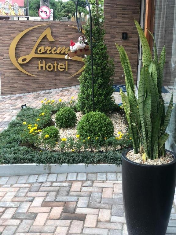 Jardim de entrada do Hotel Lorimar com plantas, flores e o letreiro dourado do hotel